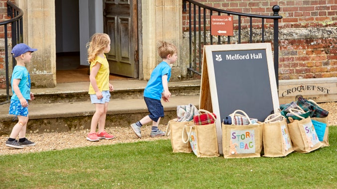 Children in the garden and bags containing picnic blankets available for visitors to borrow at Melford Hall, Suffolk